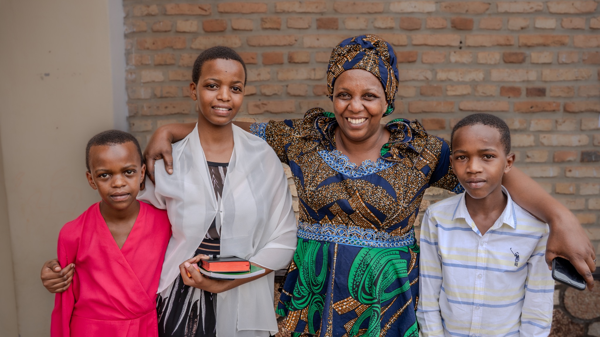 A mother standing with three children outside a brick building in Rwanda